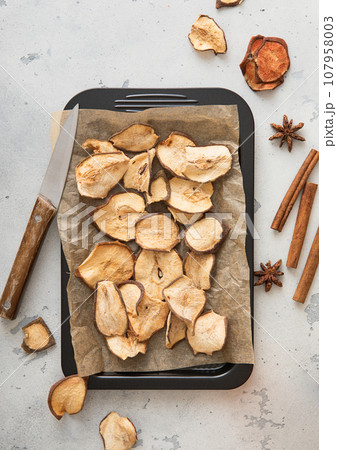 Dried pear slices on baking tray with cinnamon on light table. 107958003
