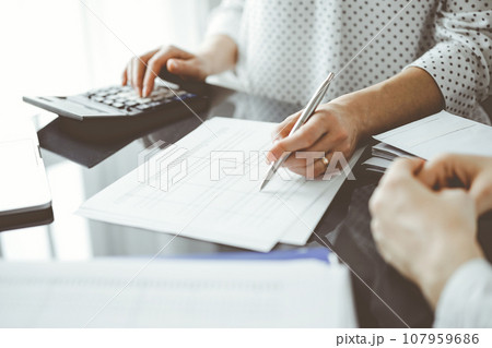 Woman accountant using a calculator and laptop computer while counting taxes for a client. Business audit and finance concepts Woman accountant using a calculator and laptop computer while counting taxes for a client. Business audit and finance concepts 107959686