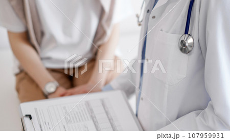 Doctor and patient discussing health exam results. Friendly physician reassuring a young woman by one hand while keeping clipboard with medical papers in another. Medicine concept Doctor and patient discussing health exam results. Friendly physician reassuring a young woman by one hand while keeping clipboard with medical papers in another. Medicine concept 107959931