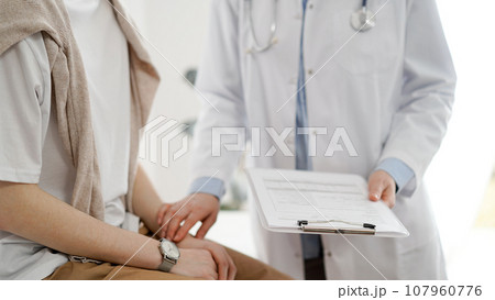 Doctor and patient in clinic. Friendly physician examining a young woman with a one hand while keeping a clipboard with medical records in another. Medicine concept 107960776
