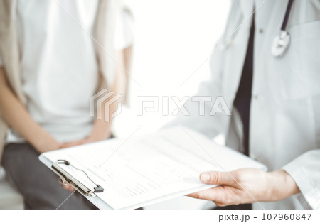 Doctor and child patient. The physician is holding clipboard with medication history records form near a boy. The concept of ideal health in medicine 107960847