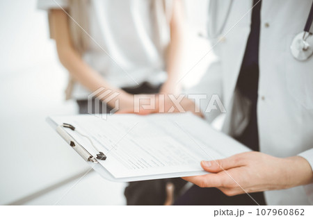 Doctor and child patient. The physician is holding clipboard with medication history records form near a boy. The concept of ideal health in medicine Doctor and child patient. The physician is holding clipboard with medication history records form near a boy. The concept of ideal health in medicine 107960862
