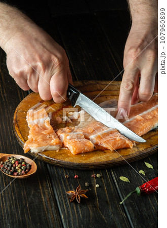 The cook cuts fresh red fish with a knife on a wooden cutting board. Homemade delicious fish dish according to an old recipe 107960899