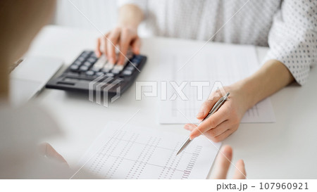 Accountant using a calculator and laptop computer for counting taxes with a client or a colleague at white desk in office. Teamwork in business audit and finance Accountant using a calculator and laptop computer for counting taxes with a client or a colleague at white desk in office. Teamwork in business audit and finance 107960921