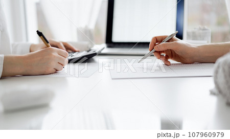 Two accountants using a laptop computer and calculator for counting taxes at white desk in office. Teamwork in business audit and finance 107960979