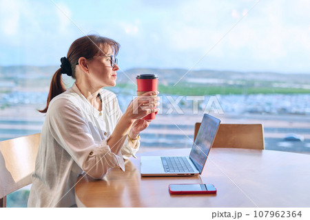 Middle aged woman in airport cafe working with laptop computer 107962364