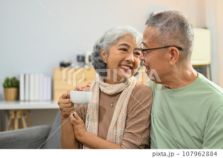 Image of happy elderly couple drinking coffee chatting spending time together at home Image of happy elderly couple drinking coffee chatting spending time together at home 107962884