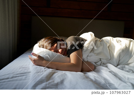 Female is sleeping cozily on a bed at the bedroom. 107963027