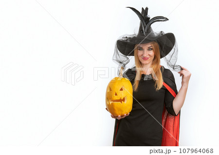 Dissatisfied young woman in witch hat with jack-o-lantern in her hands. Black clothes. Halloween party. White background, space for text 107964068