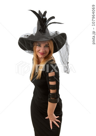 Attractive sexy woman in black witch hat and dress looking in camera. Halloween party, white background. Young witch, vertical frame 107964069
