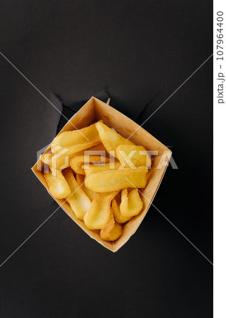 French fries sticks out through torn holes in black paper background. Street food concept 107964400