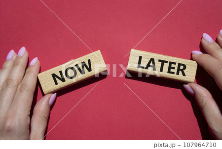 Now vs Later symbol. Concept word Now vs Later on wooden blocks. Businessman hand. Beautiful red background. Business and Now vs Later concept. Copy space 107964710