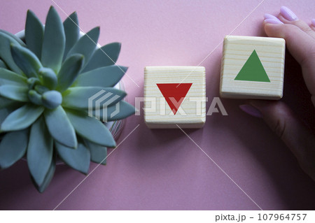 Interest rate symbol. Businessman hand is making a choice between two cubes with arrow going down and arrow going up. Beautiful pink background with succulent plant. Business concept. Copy space. Interest rate symbol. Businessman hand is making a choice between two cubes with arrow going down and arrow going up. Beautiful pink background with succulent plant. Business concept. Copy space. 107964757