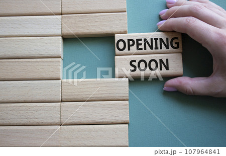 Opening soon symbol. Concept word Opening soon on wooden blocks. Businessman hand. Beautiful grey green background. Business and Opening soon concept. Copy space Opening soon symbol. Concept word Opening soon on wooden blocks. Businessman hand. Beautiful grey green background. Business and Opening soon concept. Copy space 107964841