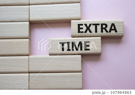 Extra time symbol. Concept word Extra time on wooden blocks. Beautiful pink background. Business and Extra time concept. Copy space 107964863