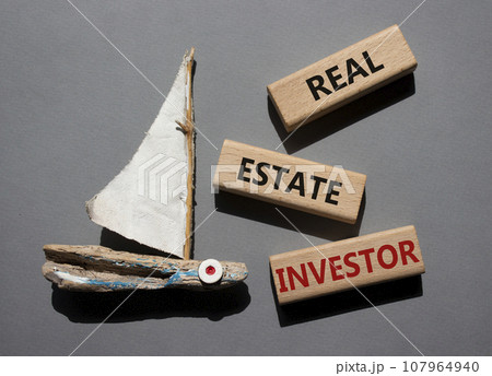 Real Estate Investor symbol. Wooden blocks with words Real Estate Investor. Beautiful grey background with boat. Business and Real Estate Investor concept. Copy space. 107964940