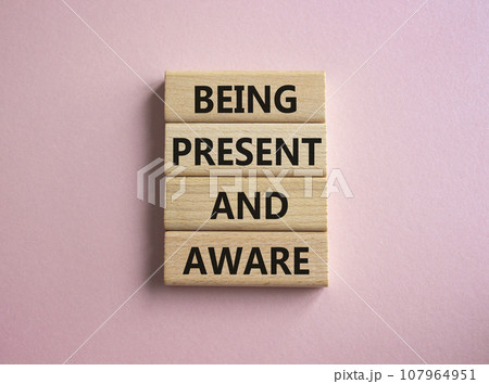 Being Present and Aware symbol. Wooden blocks with words Being Present and Aware. Doctor hand. Beautiful pink background. Psychology and Being Present and Aware concept. Copy space. 107964951
