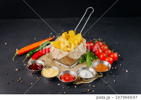 Tasty French fries served with diferent dip souces and vegetables on dark background 107966697