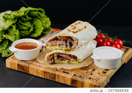 Tasty beef shawarma with fresh salad and vegetables lying on wooden board. Traditional arab dishes Tasty beef shawarma with fresh salad and vegetables lying on wooden board. Traditional arab dishes 107966698