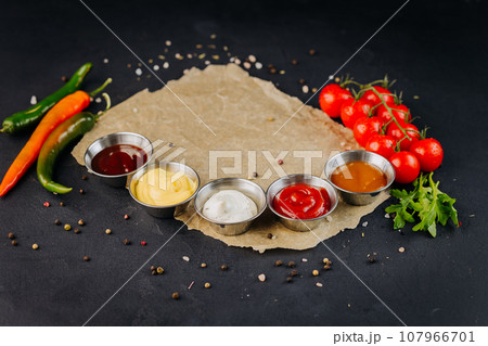 Set of different bowls of various dip sauces, on dark background served with vegetable Set of different bowls of various dip sauces, on dark background served with vegetable 107966701