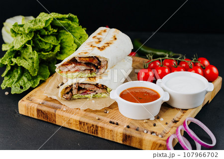 Turkish Doner Kebab on lavash with beef, fresh salad and vegetables lying on board with sauces Turkish Doner Kebab on lavash with beef, fresh salad and vegetables lying on board with sauces 107966702