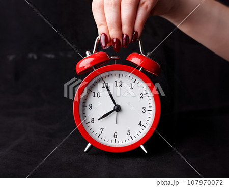 Female arm hold up red alarm clock 107970072