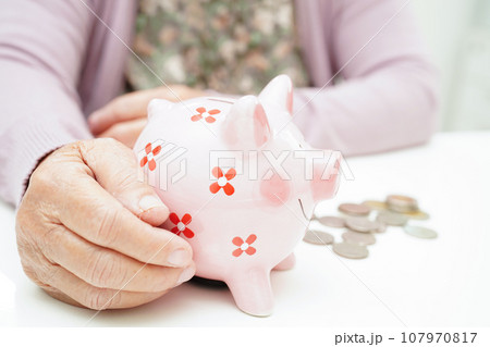 Retired elderly woman counting coins money with piggy bank and worry about monthly expenses and treatment fee payment. 107970817