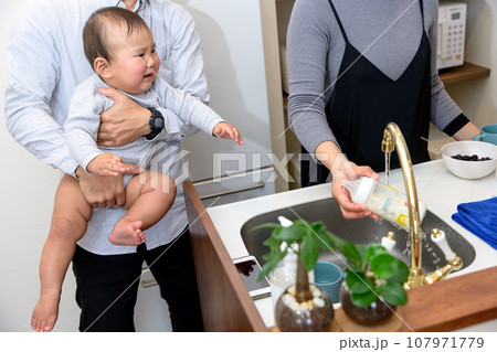 父親に抱っこしてもらい赤ちゃんに冷やしたミルクを飲ませる母親　あやす　乳幼児　イクメン　0歳乳幼児 107971779