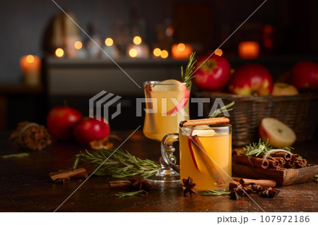 Mulled cider with apples, cinnamon, rosemary, and anise on a background of burning candles. Mulled cider with apples, cinnamon, rosemary, and anise on a background of burning candles. 107972186