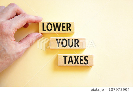 Lower your taxes symbol. Concept words Lower your taxes on wooden blocks on a beautiful white table white background. Businessman hand. Business tax lower your taxes concept. Copy space. Lower your taxes symbol. Concept words Lower your taxes on wooden blocks on a beautiful white table white background. Businessman hand. Business tax lower your taxes concept. Copy space. 107972904