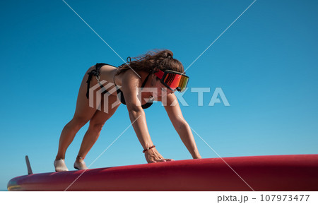 athletic girl in a swimsuit doing stretching on a sup-board in summer athletic girl in a swimsuit doing stretching on a sup-board in summer 107973477