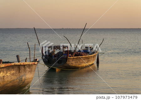 African fishing boats stranded in the sand off the coast at low tide at sunset African fishing boats stranded in the sand off the coast at low tide at sunset 107973479