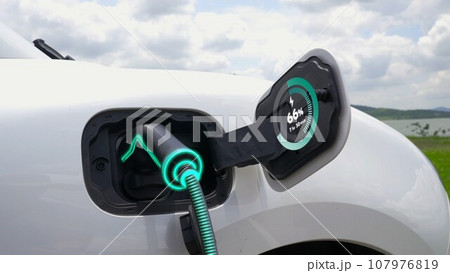 Electric car plugged in with charging station with nature background. Peruse 107976819
