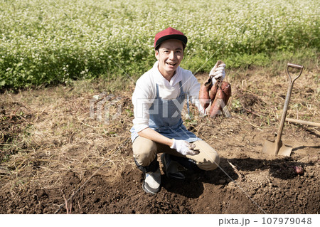 掘り出したサツマイモを持って笑う男性 107979048