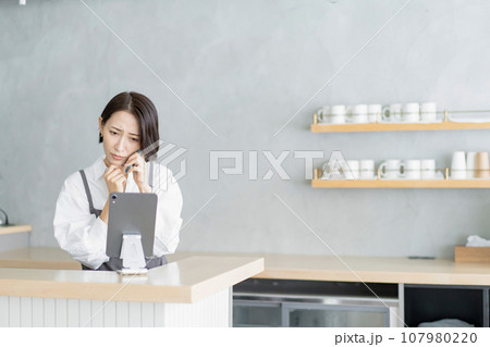 困った様子で電話対応するエプロン姿の女性 107980220