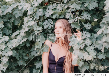Woman travel winery. Portrait of happy woman holding glass of wine and enjoying in vineyard. Elegant young lady in hat toasting with wineglass smiling cheerfully enjoying her stay at vineyard. 107980371