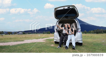 Car road trip traveling couple tourists enjoying mountain view relaxing on car. Happy Asian woman, women girlfriends smiling on car 107980839