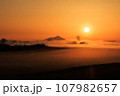 霧の湿原に朝日を浴びて立つ山 107982657