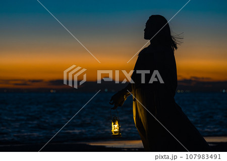 夕暮れのグラデーションのなか、ランタン片手に歩む若い女性 夕暮れのグラデーションのなか、ランタン片手に歩む若い女性 107983491