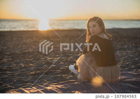 夕暮れの海岸で座っている女性のふりかえり 夕暮れの海岸で座っている女性のふりかえり 107984563