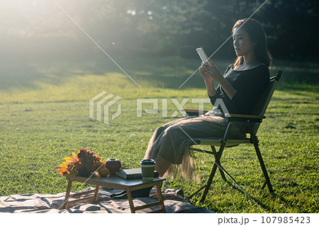 緑豊かな公園で逆光のなかスマートフォンを見る若い女性 緑豊かな公園で逆光のなかスマートフォンを見る若い女性 107985423