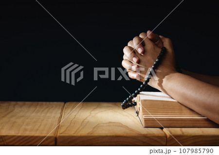 Spirituality, Religion and Hope Concept. Person Praying by Holy Bible and Bead on Desk. Symbol of Humility, Supplication, Believe and Faith for Christian People. Dark Tone. 107985790