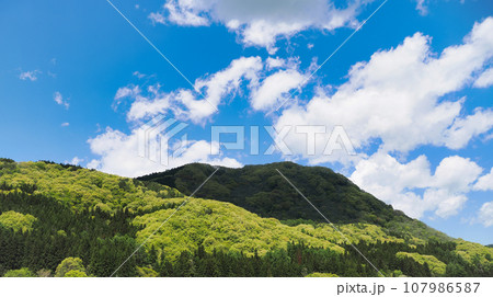 快晴の青空と雲、新緑の山並みの風景 107986587