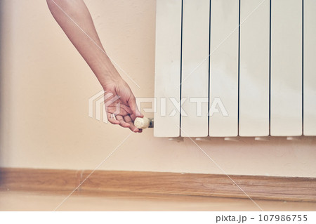 A woman's hand regulating the temperature on the radiator. The concept of the energy crisis in Europe with space to copy. High quality photo 107986755