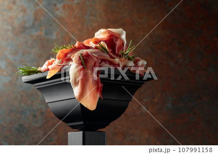Prosciutto with rosemary on a black podium. 107991158