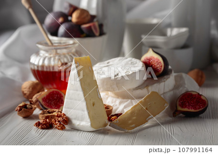 Camembert cheese with figs, walnuts, and honey on a white table. Camembert cheese with figs, walnuts, and honey on a white table. 107991164