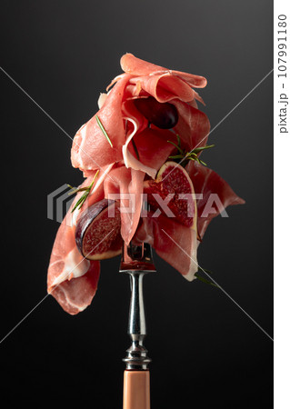 Prosciutto with figs, rosemary, and red olives on a fork. Prosciutto with figs, rosemary, and red olives on a fork. 107991180