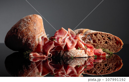 Prosciutto with ciabatta and thyme on a black background. Prosciutto with ciabatta and thyme on a black background. 107991192