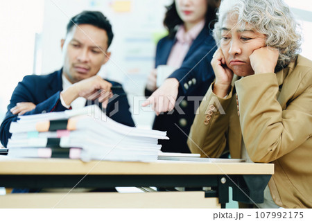 An image of an Asian male employee looking worried and sad about being scolded by his boss for failing to meet sales targets, concept of disappointment and failure in his career. 107992175