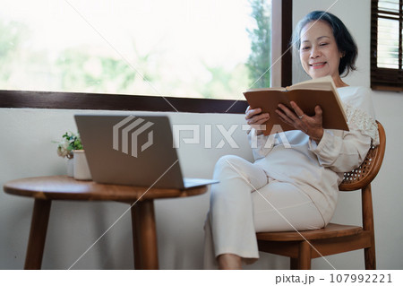 Portrait of an elderly Asian woman in a modern pose holding a memory notebook and operating a computer Portrait of an elderly Asian woman in a modern pose holding a memory notebook and operating a computer 107992221